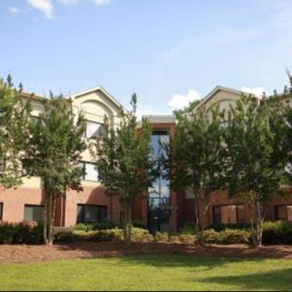 A view of a residential building surrounded by trees and a well-kept lawn under a clear sky.