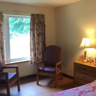 A cozy room with a window, two chairs, and a lamp on a dresser.