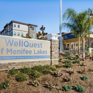 The entrance sign of WellQuest of Menifee Lakes with surrounding landscaping and a view of the building.
