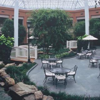 A serene indoor atrium featuring tables and chairs surrounded by lush greenery under a glass ceiling.