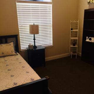 A cozy bedroom with a single bed, lamp, and shelving unit.