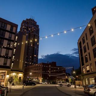 A city street at dusk with string lights illuminating the buildings.