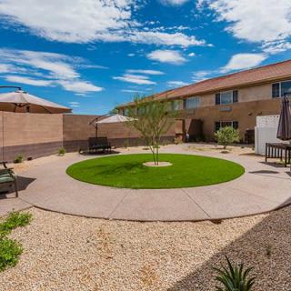 A well-maintained backyard with artificial grass, patio seating, and desert landscaping on a sunny day.