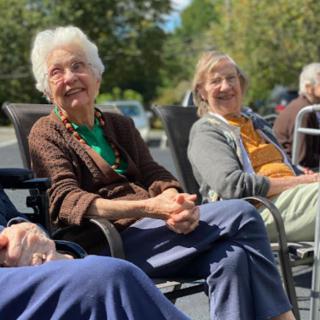 A group of elderly individuals enjoying a sunny day outdoors, sitting and smiling on chairs.
