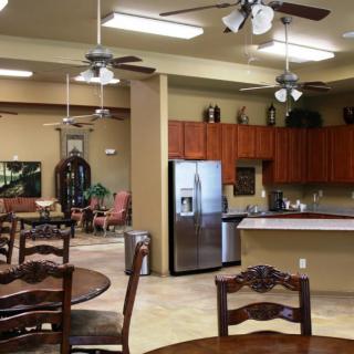 An open kitchen and dining area with wooden cabinetry, stainless steel appliances, ceiling fans, and decorative indoor plants.