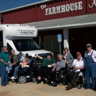 A group of people gathered outside The Farmhouse Restaurant with a wheelchair-accessible van.