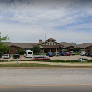 A view of a large building with a parking lot and several cars parked, seen from across the road.