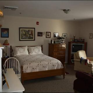 A cozy bedroom featuring a bed, television, chair, dresser, and decorative wall art.