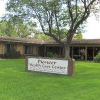 A view of the Pioneer Health Care Center with a sign in front and surrounding greenery.