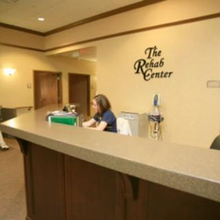 A receptionist working at a front desk in an office with a sign reading 'The Rehab Center'.