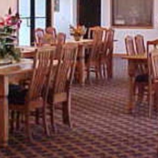 A dining area with wooden tables and chairs, featuring floral decorations and a patterned carpet.