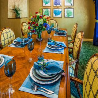 A beautifully set dining room table with blue-accented place settings and a vibrant floral centerpiece.
