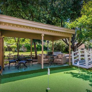 A charming backyard with a gazebo and putting green surrounded by lush trees.