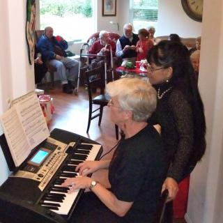 Two people performing music on a keyboard for an audience indoors.