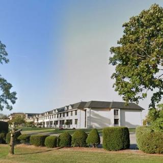 A white building surrounded by trees and bushes under a clear sky.