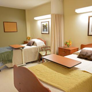 A view of a shared patient room in a hospital, featuring two beds, bedside tables, and warm-colored walls.
