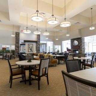 A spacious and modern lounge area with tables and chairs, featuring elegant lighting fixtures.