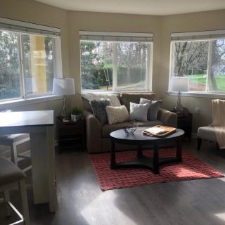 A cozy living room with ample natural light, featuring a comfortable sofa, coffee table, and large windows.