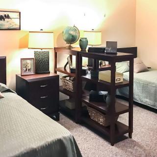 A cozy bedroom with two beds separated by a dark wooden bookshelf, featuring lamps and decorative items.