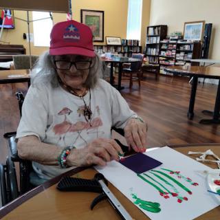 An elderly woman engages in a creative crafting activity at a senior center, using colorful materials.