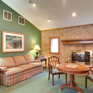 A cozy living room with a green accent wall, featuring a sofa, fireplace, table, chairs, and decorative elements.