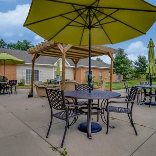 A sunny day on a patio with tables, chairs, and umbrellas next to a brick building.