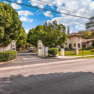 A picturesque gated entrance leads to a property lined with trees under a partly cloudy sky.