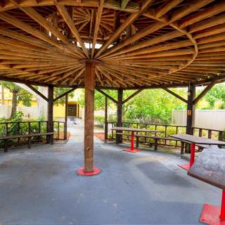 A spacious wooden gazebo with a circular roof, featuring benches and surrounded by greenery.