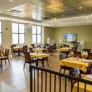 A spacious dining room with neatly arranged tables covered in yellow tablecloths, set beneath elegant chandeliers.