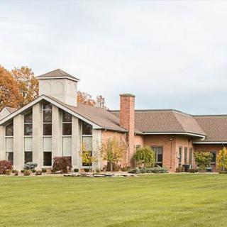 A modern residential house with a large lawn and autumn trees surrounding it.