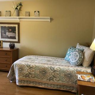A cozy bedroom with a single bed, nightstand, and dresser, featuring decorative pillows and a lamp.