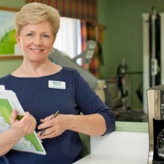 A woman smiling while holding a clipboard and pen in an office setting.