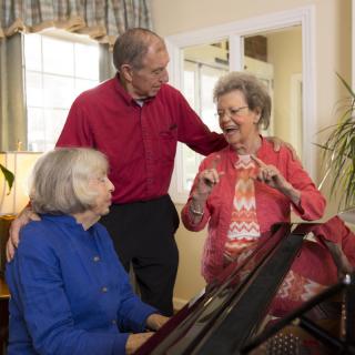 A group of seniors enjoying a musical moment around the piano indoors.
