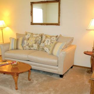 A cozy living room with a beige sofa, patterned cushions, a wooden coffee table, and warm lighting.