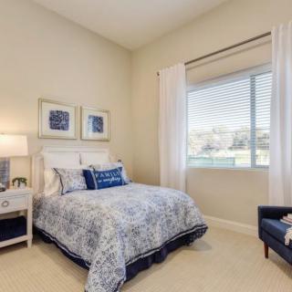 A cozy bedroom featuring a comfortable bed with patterned bedding, a side table with a lamp, and large window with curtains.