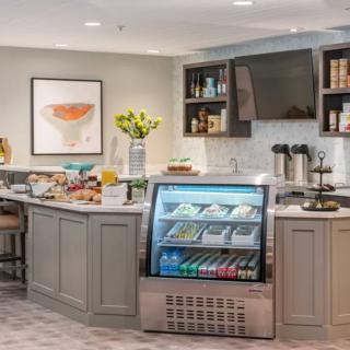 A cozy cafe interior featuring a counter with a beverage cooler, snacks, and a coffee station.
