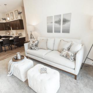 A modern and minimalist living room featuring a white sofa, decorative pillows, a small coffee table, and wall art in neutral tones.