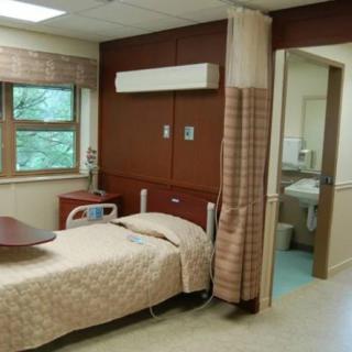 A clean and well-organized hospital room equipped with a bed, window, and privacy curtain.