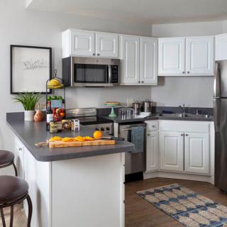 A modern kitchen with white cabinets and stainless steel appliances, featuring a countertop adorned with fresh fruits and decor.