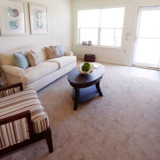 A cozy living room with a sofa, armchair, coffee table, and large windows.
