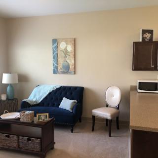 A cozy living room featuring a blue sofa with a blanket and pillow, a side chair, artwork on the wall, a lamp, and a coffee table.