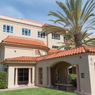 A Mediterranean-style building with a tiled roof, surrounded by palm trees and grass.