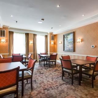 A cozy dining room with multiple tables and chairs, accented by warm lighting and a carpeted floor.