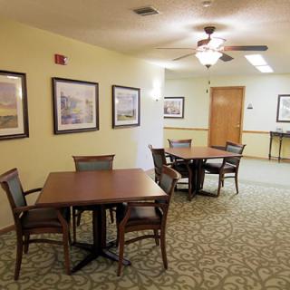 A well-lit room featuring multiple tables and chairs, artwork on the walls, and a carpeted floor.