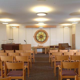 An interior view of a meeting room with chairs arranged facing a podium and a stained glass window.