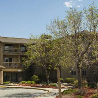A residential apartment complex surrounded by trees and landscaping under a clear blue sky.