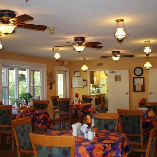 A cozy dining room with tables and chairs, featuring ceiling fans and warm lighting.
