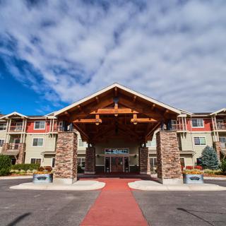 A welcoming entrance to a hotel with a wooden canopy and stone pillars under a partly cloudy sky.