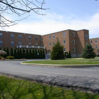 A large brick building with a circular driveway and landscaped greenery under a clear sky.