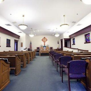 Interior view of a church with wooden pews and a cross at the altar.